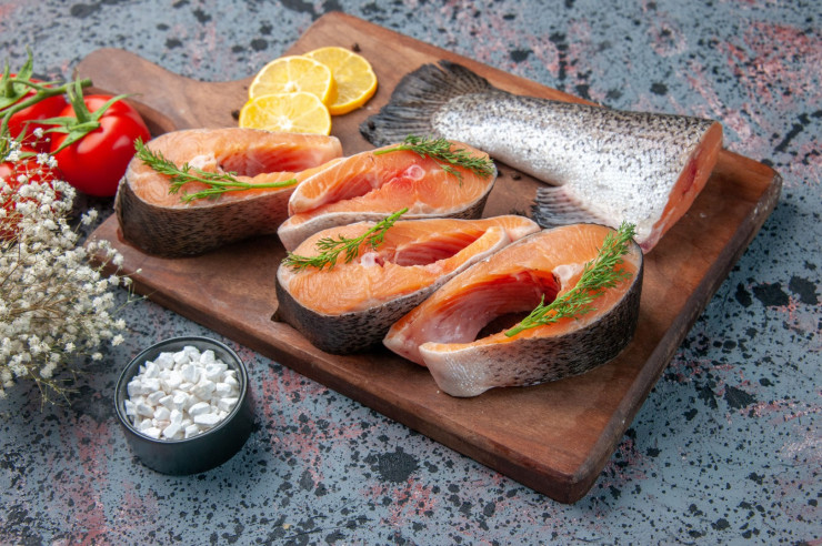 side-view-raw-fishes-lemon-slices-greens-pepper-wooden-cutting-board-knife-fresh-foods-blue-black-mix-colors-table (1)