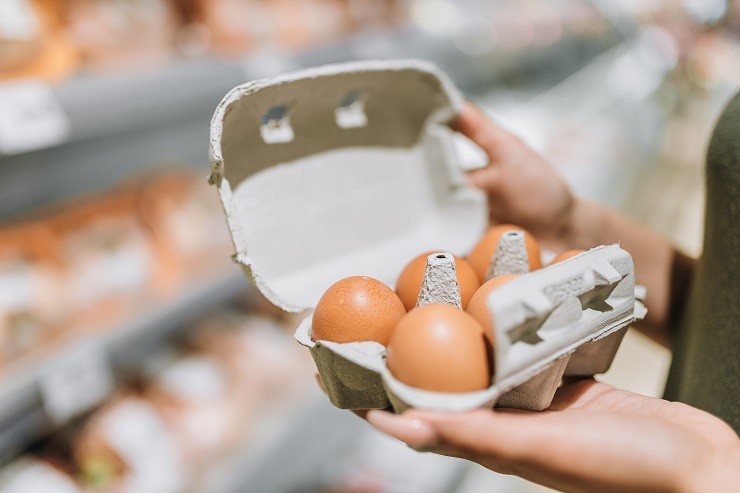 young-woman-in-store-holding-cardboard-of-six-organic-eggs